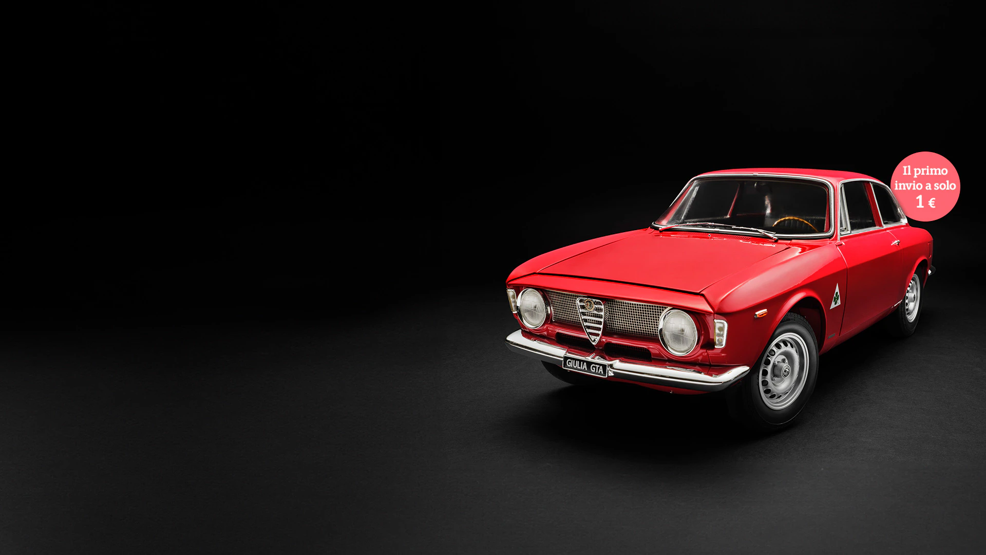 Immagine di un’auto d’epoca Alfa Giulia Sprint rossa su sfondo nero. L’immagine include il testo promozionale: “Il primo invio a solo 1€”