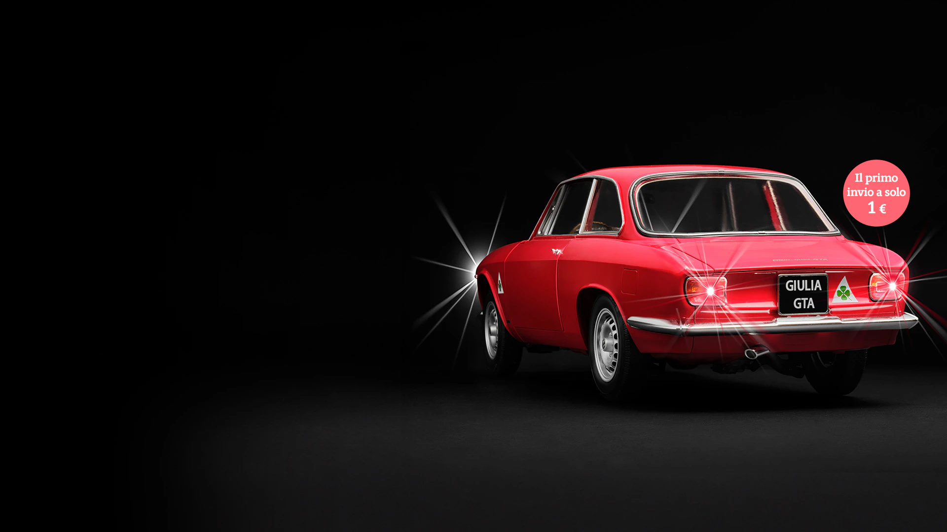Immagine di un’auto d’epoca Alfa Giulia Sprint rossa su sfondo nero. L’immagine include il testo promozionale: “Il primo invio a solo 1€”